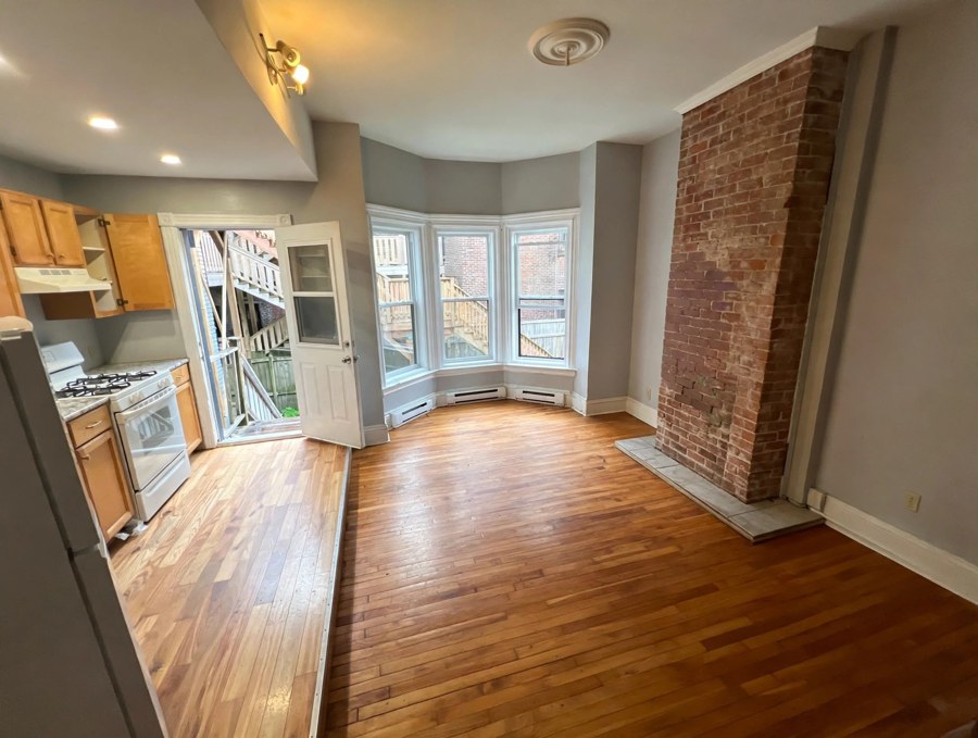 Living and kitchen area with bay windows and exposed brick
